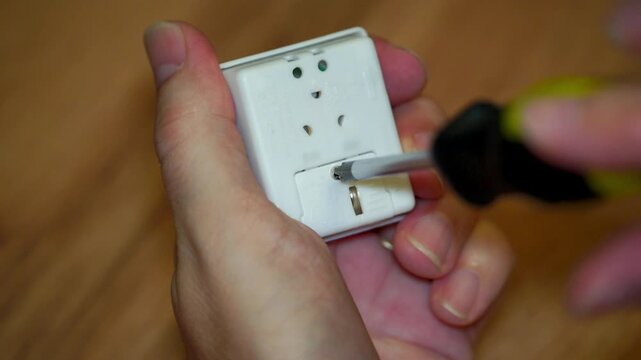 Close-up of hands using a screwdriver to unscrew a small electronic device to reveal internal battery.