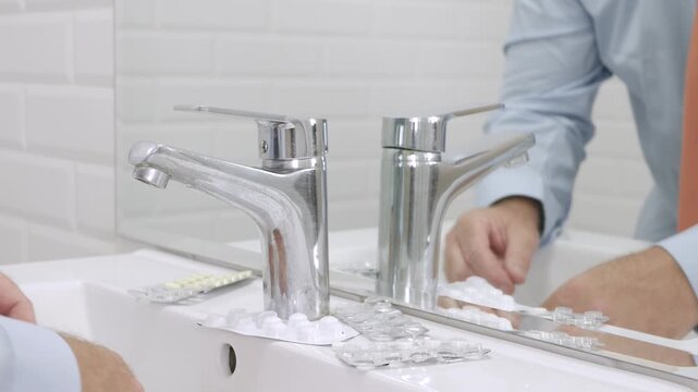 Blurred Shooting with a Sick and Suffering Man in Front of the Bathroom Mirror taking from the Sink Medical Pills.