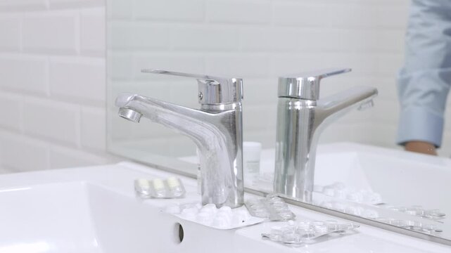 Blurred Shooting with a Sick and Nervous Person in Bathroom Looking in the Mirror with Many Medical Pills on the Sink.