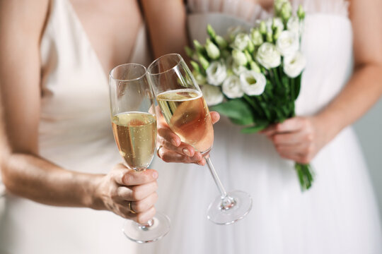 Lesbian wedding. Brides with glasses of sparkling wine on light grey background, closeup