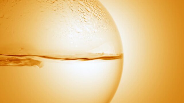 Enlarged view of bright clear fluid boiling in a round-bottom flask, producing bubbles and condensation on its wall on orange ramp background | Orange hydrosol cosmetic formulation design concept
