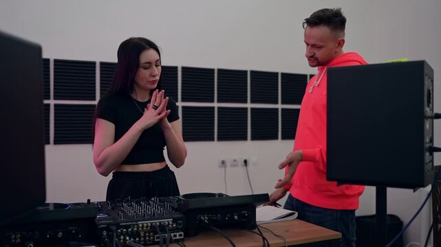 DJ teaches a girl how to mix tracks during his lesson. DJ courses hobby for adults. Music dj producer showing to young woman how to adjust volume on sound mixer in music studio.