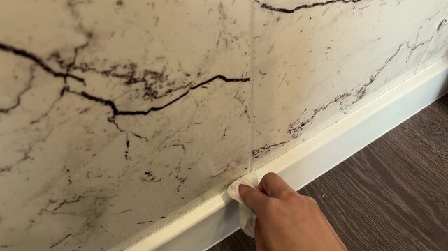 A hand wipes a dirty baseboard with a cloth, home cleaning, household maintenance, sanitation, everyday chores, interior care.