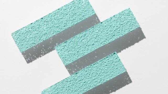 View from above shot of light cyan powder sifted through a three stripe stencil on transparent surface, casting moving shadow on a light grey backdrop