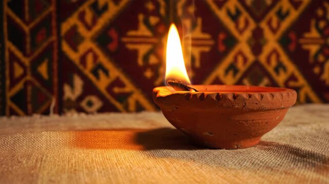 Burning clay diya on burlap with traditional pattern background.