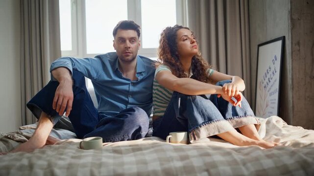 Sad couple sitting bed after argument. Upset man woman ignoring each other home.