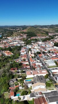 Registro a&eacute;reo de cidade de m&eacute;dio porte com avenida principal, resid&ecirc;ncias e estabelecimentos, mostrando a distribui&ccedil;&atilde;o urbana e o ambiente cercado por eleva&ccedil;&otilde;es.