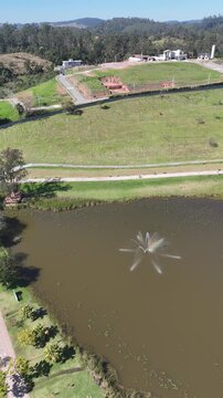 Imagem a&eacute;rea do Parque do Lago em Guararema, com chafariz, vias sinuosas, &aacute;reas verdes e relevo montanhoso compondo uma paisagem tur&iacute;stica e tranquila.