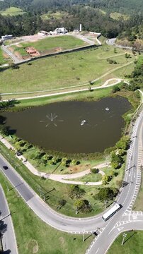 Imagem de drone do Parque do Lago, em Guararema, mostrando lago ornamental com chafariz, vias curvas, gramados e relevo montanhoso em cen&aacute;rio de lazer e natureza.