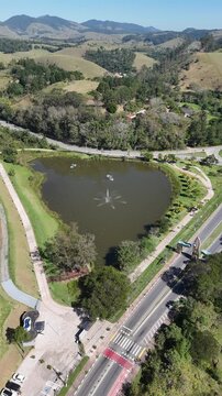 Lago com fonte visto por drone no Parque do Lago, em Guararema, cercado por gramados, &aacute;rvores e vias sinuosas, representando turismo, lazer e contato com a natureza.
