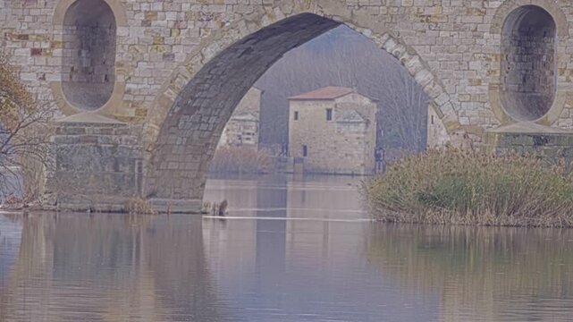 Masonry Pointed arch Stone bridge (Puente de Piedra) across the river Duero in Zamora, Castile-Leon, Spain. Reflection in the water. Autumn nature. Overcast.