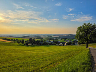 Obraz premium rolling green countryside with village at golden sunset under a colorful evening sky