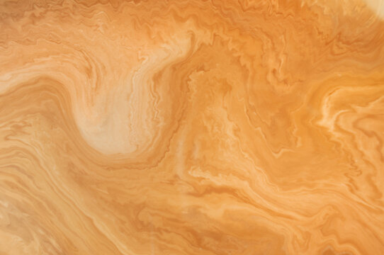 Waves of orange and beige colors swirl together on a smooth surface