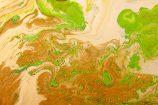Swirls of brown and green paint mix together on a canvas