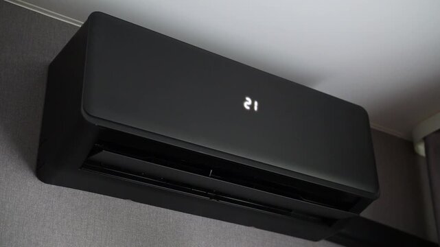 Black modern air conditioning unit mounted on wall. Sleek design with horizontal vents. Minimalist interior setting. Clean lines and matte finish. Fits contemporary home or office space