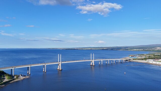 Inverness, Scotland, British city shines at daytime, overlooking the sea beneath drifting clouds, with an elegant bridge connecting scenic riverbanks beautifully.