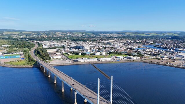 Inverness, Scotland, British city at daytime features an elegant bridge from the left, overlooking the sea beneath soft white clouds beautifully.