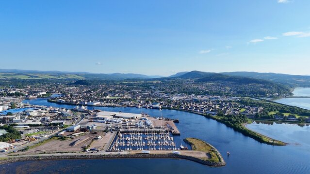 Aerial view of Inverness, Scotland, British city, right side with wide flat lands and hills, left side with river joining sea and boats.