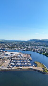 Aerial view of Inverness, Scotland, British city, right side showing flat land and hills, left side showing river meeting sea with boats.