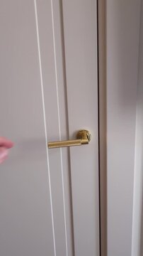 Man's hand gripping a golden handle to open and close a white interior door, revealing a glimpse of a modern kitchen or studio apartment before shutting it again with a gentle click