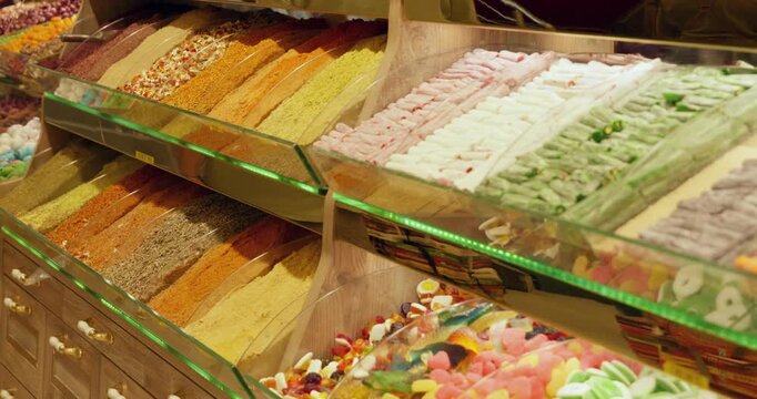 Colorful rows of traditional Turkish delight confections arranged in glass display cases with LED lighting, showcasing variety of flavors, textures, and vibrant hues in middle eastern market setting.