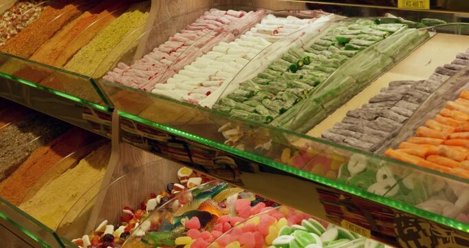Vibrant assortment of Turkish delight confections arranged in glass display cases at market stall, showing pink, green, orange, white varieties with traditional presentation.