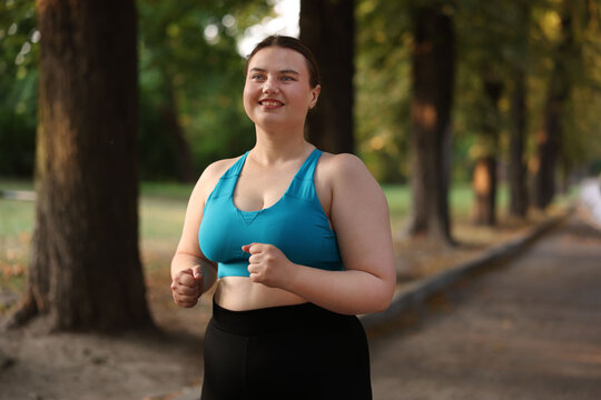 Smiling overweight woman running in park on summer day