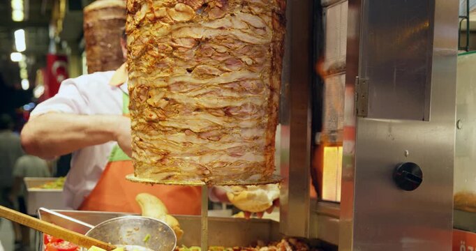 Professional cook cuts thin slices from rotating meat column on vertical spit in commercial kitchen, preparing traditional Middle Eastern shawarma for service.