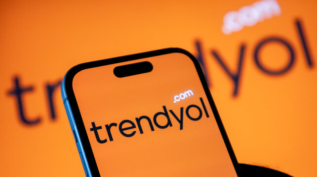 A close up of a hand holding an iphone 14 pro with trendyol com logo on screen and background.