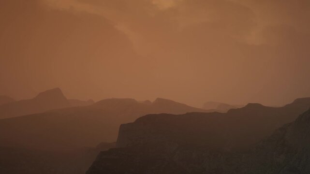 Mountains appear in silhouette against an orange sky at sunset. The scene shows layers of distant peaks, creating a simple yet striking visual of nature.