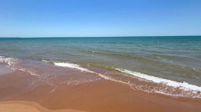 Gentle waves rolling onto a sandy beach on the Mediterranean coast of Sicily during a hot summer day. Slow camera pan reveals turquoise sea, golden shoreline and peaceful coastal scenery.