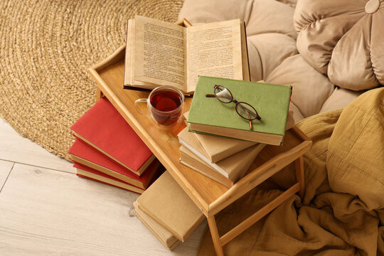 Cozy reading scene with open book, eyeglasses, and tea on a wooden tray next to a stack of red books