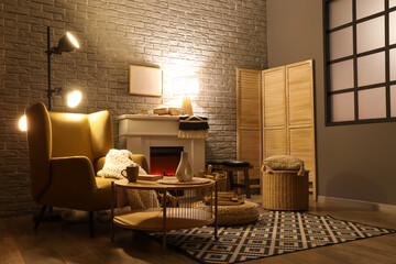 Obraz premium Interior of living room with fireplace, armchair and glowing lamps