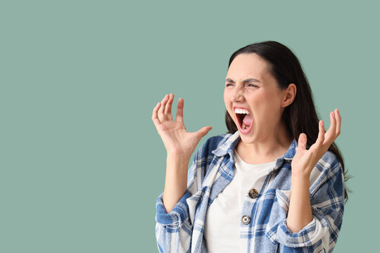 Angry young woman screaming on green background