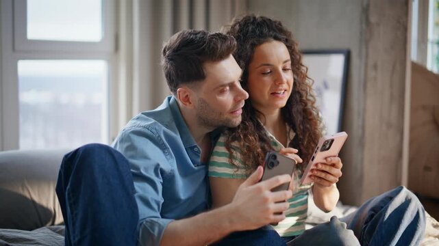 Young couple sharing smartphones home bed. Comparing two phones cozy weekend.