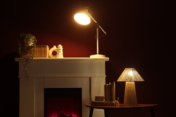 Obraz premium Interior of stylish room with fireplace, coffee table and glowing lamp near red wall at night