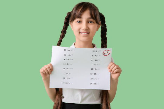 Happy schoolgirl holding paper with good results of school test on green background