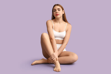 Fototapeta premium Beautiful young woman after depilation sitting on purple background