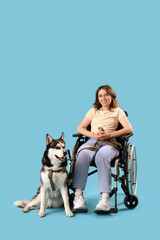Young woman in wheelchair and with husky dog on light blue background © Pixel-Shot