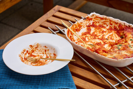 Leftover baked gnocchi in tomato sauce beside empty plate with used fork on table