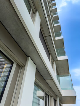 Modern building exterior with balconies. A tall building shows its white and glass balconies against a blue sky on a sunny day.