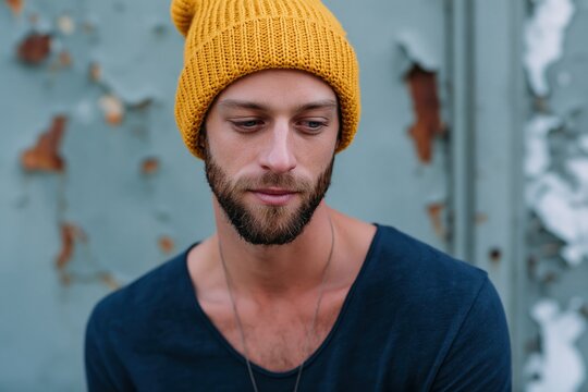 Closeup bearded man wearing yellow beanie with thoughtful expression against textured peeling wall for lifestyle portrait background
