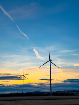 Turbines at sunset. Two wind turbines stand tall against a sunset sky in a rural area. The colorful clouds create a scenic view.