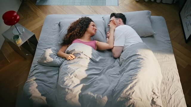Happy couple lying bed morning. Man caressing woman face cozy weekend bedroom.
