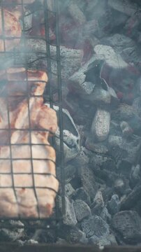 Charcoal fire grills raw pork steaks outdoors for a summer barbecue meal. Vertical static overhead shot.
