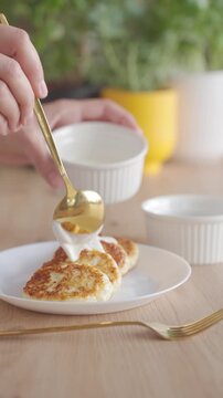 Cream is spooned onto cottage cheese pancakes on plate. Concept of homemade breakfast and simple serving