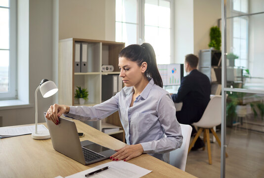 Woman working on laptop at office desk. Bright office with coworker in background, analysis charts on computer for marketing, reports and presentations. Concept of productivity and focus.