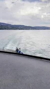 Boat Trail on a Lake Seen From a Ferry Deck With Hills and Clouds in Switzerland