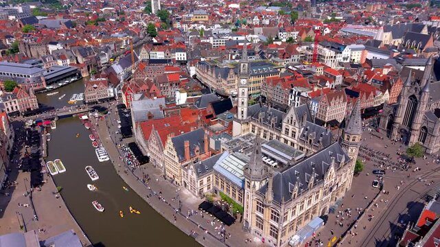 Aerial wide angle panoramic view of the historic old post office building and Saint Nicholas Church overlooking a scenic river canal with tour boats in Ghent city center under a bright summer sky
