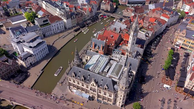 Aerial wide angle panoramic view of the magnificent historic old post office building looking down at a winding river canal with tour boats and a busy public square in Ghent city center